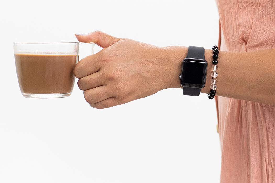 The Benefits of Wearing Shungite. Woman holding cup of coffee while wearing a Shungite Bracelet and an Apple Watch.