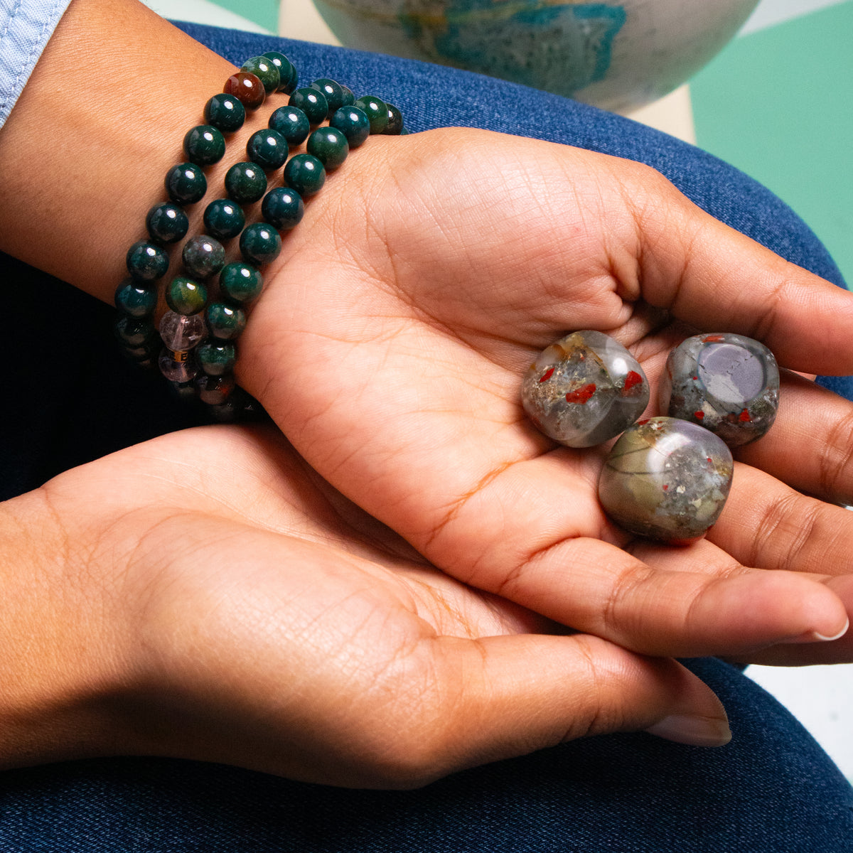Biracial woman wearing 3 genuine Bloodstone crystal bracelets and holding 3 Bloodstone crystals in her upturned open palm by Energy Muse