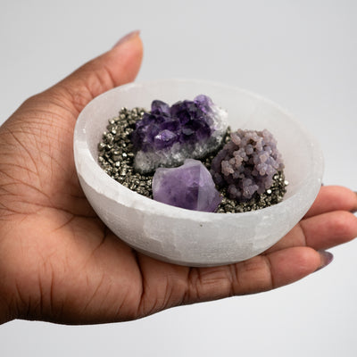 Woman holding medium sized Selenite charging bowl that's filled with Pyrite chips, Amethyst cluster, and Grape Agate by Energy Muse