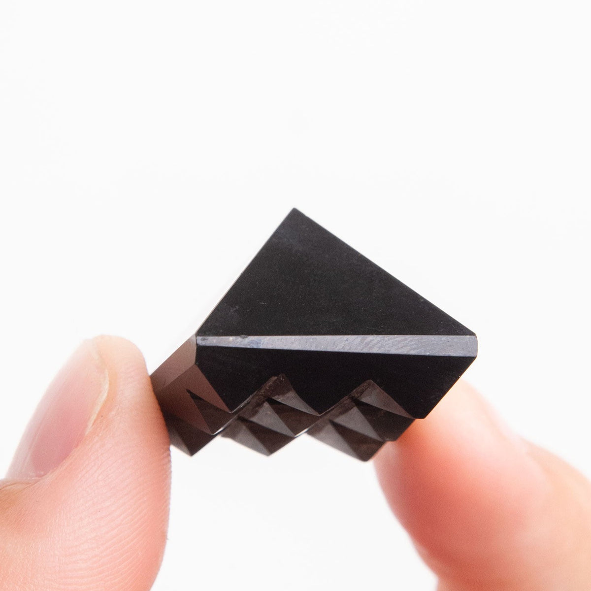 hand holding genuine Shungite pyramid with unique 9-pyramid carving on the base by Energy Muse
