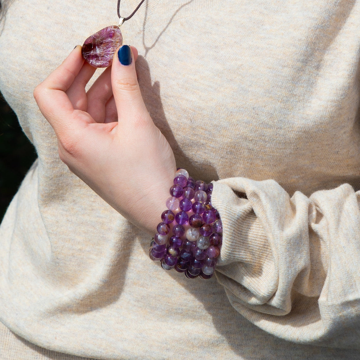 Woman wearing 5 Super Seven crystal bracelets and holding a Super Seven pendant necklace by Energy Muse