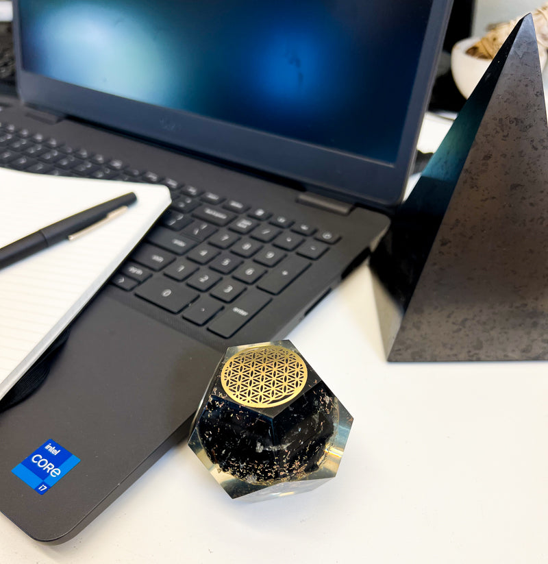 Stylized view of Black Tourmaline Orgone Dodecahedron with metal Flower of Life decor by laptop and extra large Shungite pyramid by Energy Muse