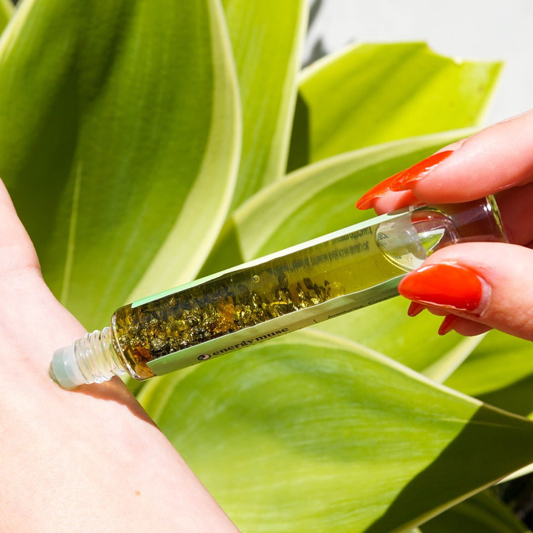 Woman rolling Money Magnet Oil Roller by Energy Muse featuring genuine Pyrite, Aventurine and Citrine crystals, plus organic cinnamon, five finger grass and basil oils on her left wrist.