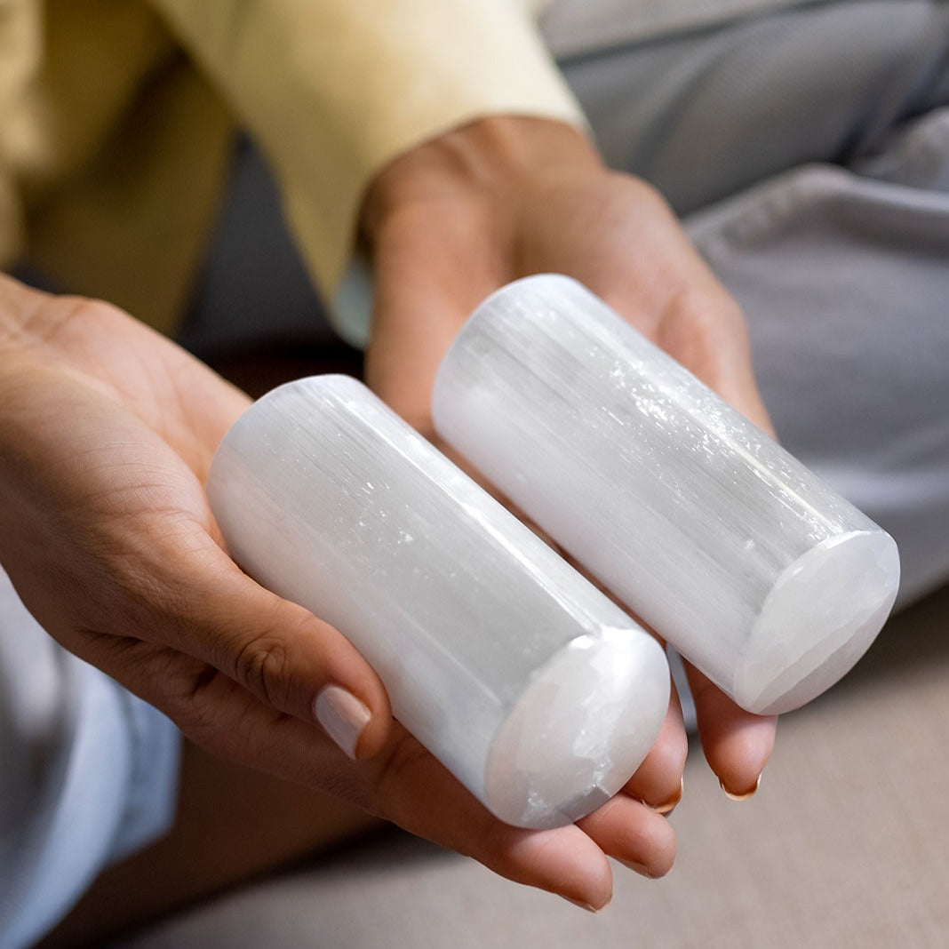 A woman sitting cross-legged on the floor holding 2 genuine Selenite Satin Spar harmonizers for meditation by Energy Muse