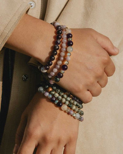 Close up of young non-binary Latino person's two hands and wrists, wearing seven genuine crystal bracelets, featuring the new Miracles Bracelet by Energy Muse