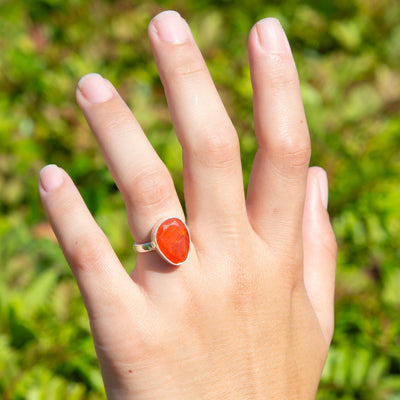 Woman wearing genuine faceted Carnelian statement crystal ring by Energy Muse on her ring finger of her left hand in nature.