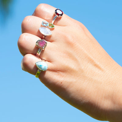 Woman wearing genuine Larimar teardrop shaped crystal ring in sterling silver, watermelon tourmaline slice ring, moonstone, peridot and topaz ring and garnet ring by Energy Muse