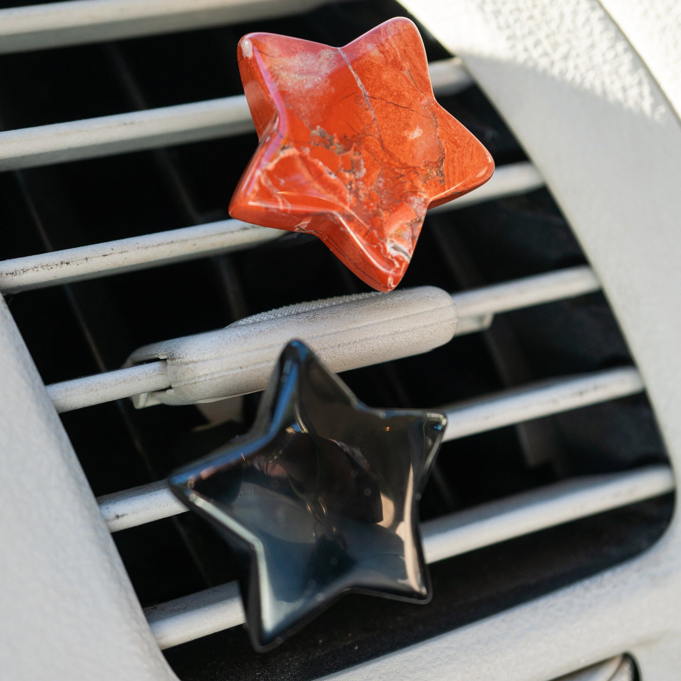 close up of a star-shaped Red Jasper car air vent clip and star-shaped Black Obsidian car air vent clip on a car air vent by Energy Muse