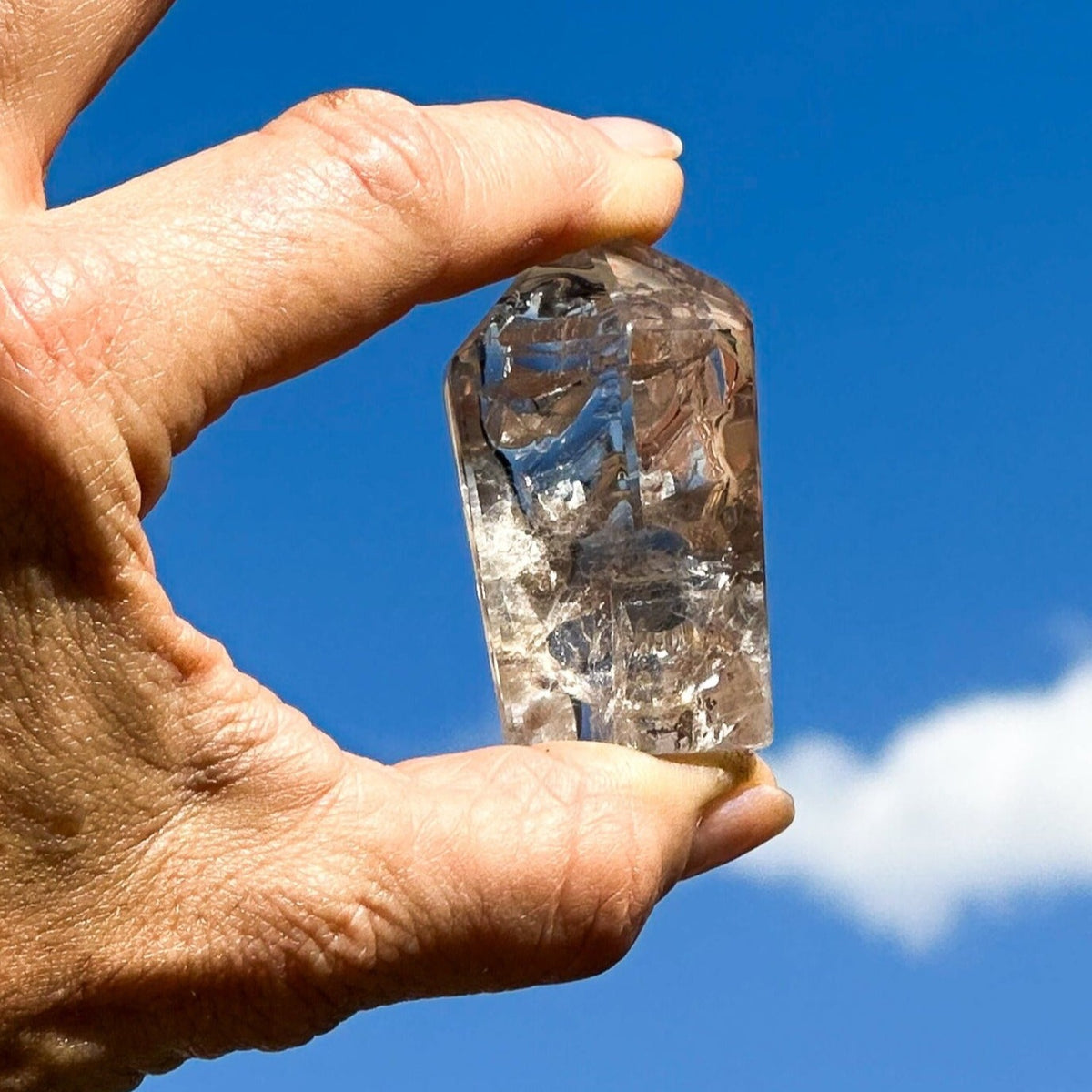 White woman wearing several crystal bracelets, holding genuine Manifester crystal freeform up to the sky by Energy Muse