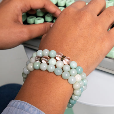 Close up of young woman's wrist typing on mint-colored typewriter and wearing 3 Energy Muse Amazonite stretch bracelets.