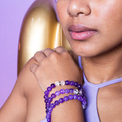 Young biracial woman wearing three Energy Muse crystal bead bracelets and wearing a lilac tank top with lavender background