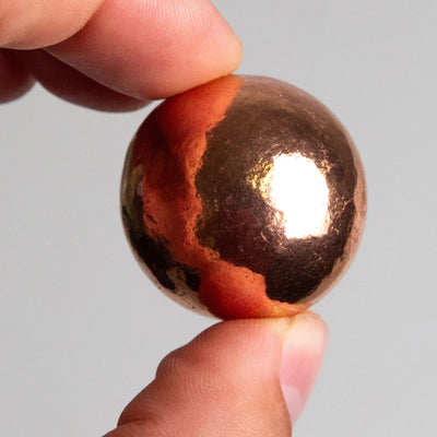 Man holding Copper Sphere by Energy Muse in index finger and thumb to show size