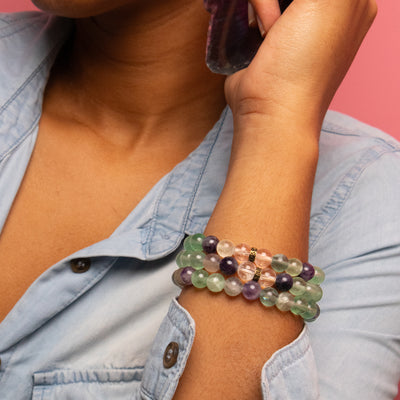Close up view of woman holding arm up and wearing three Fluorite bracelets by Energy Muse