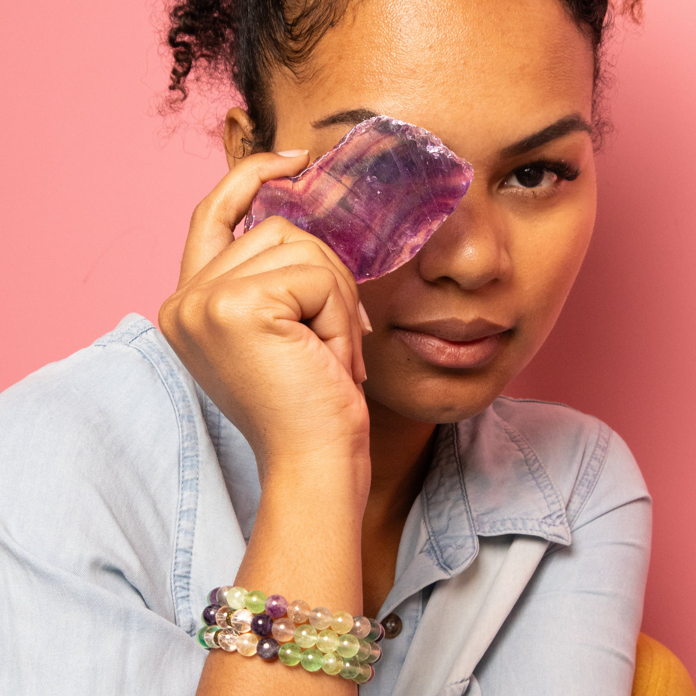 Young biracial woman wearing 3 genuine Fluorite bead stretch bracelets and holding up a banded semi-translucent Fluorite Crystal Slab by Energy Muse