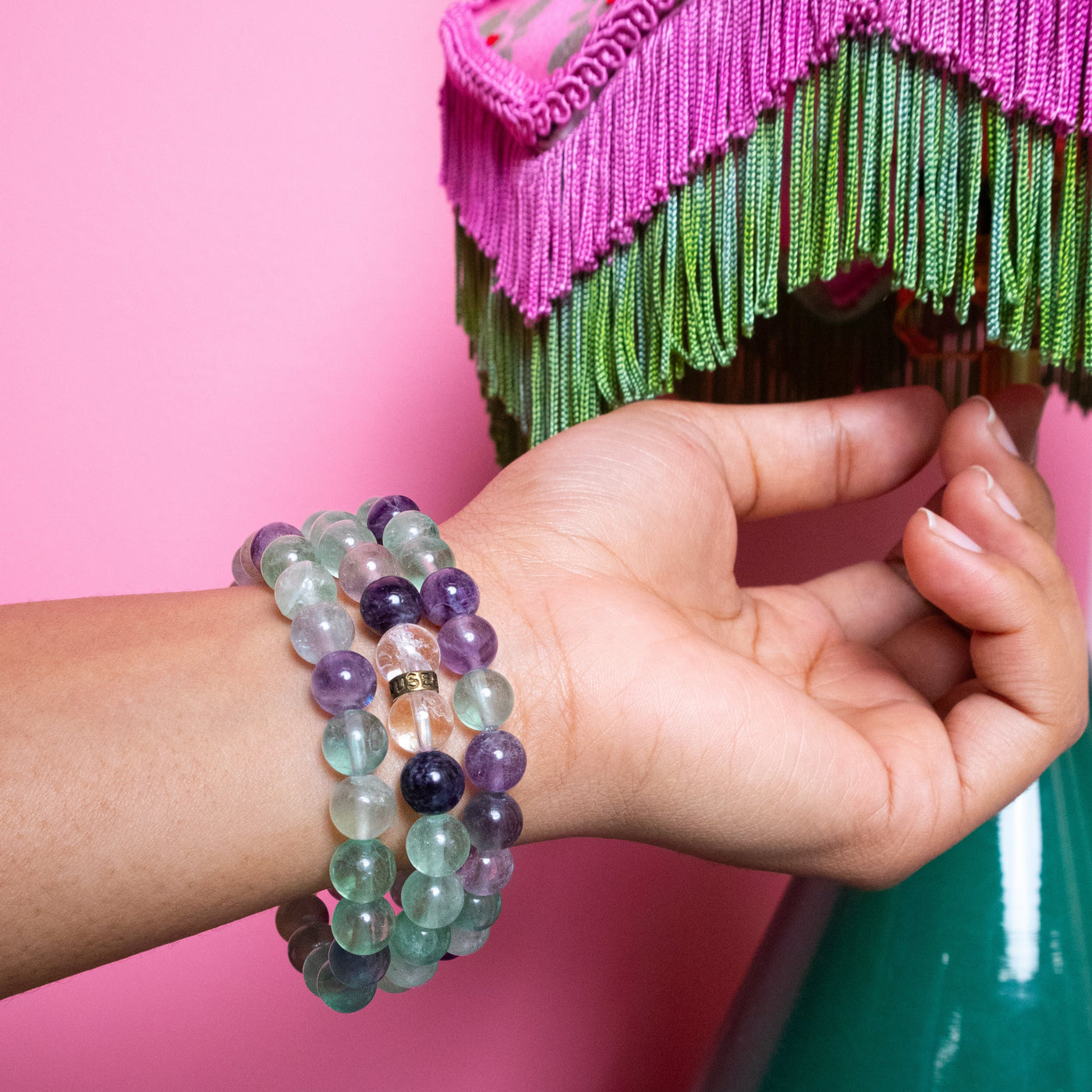 Close up of woman wearing three Fluorite bracelets near a tasseled lampshade by Energy Muse