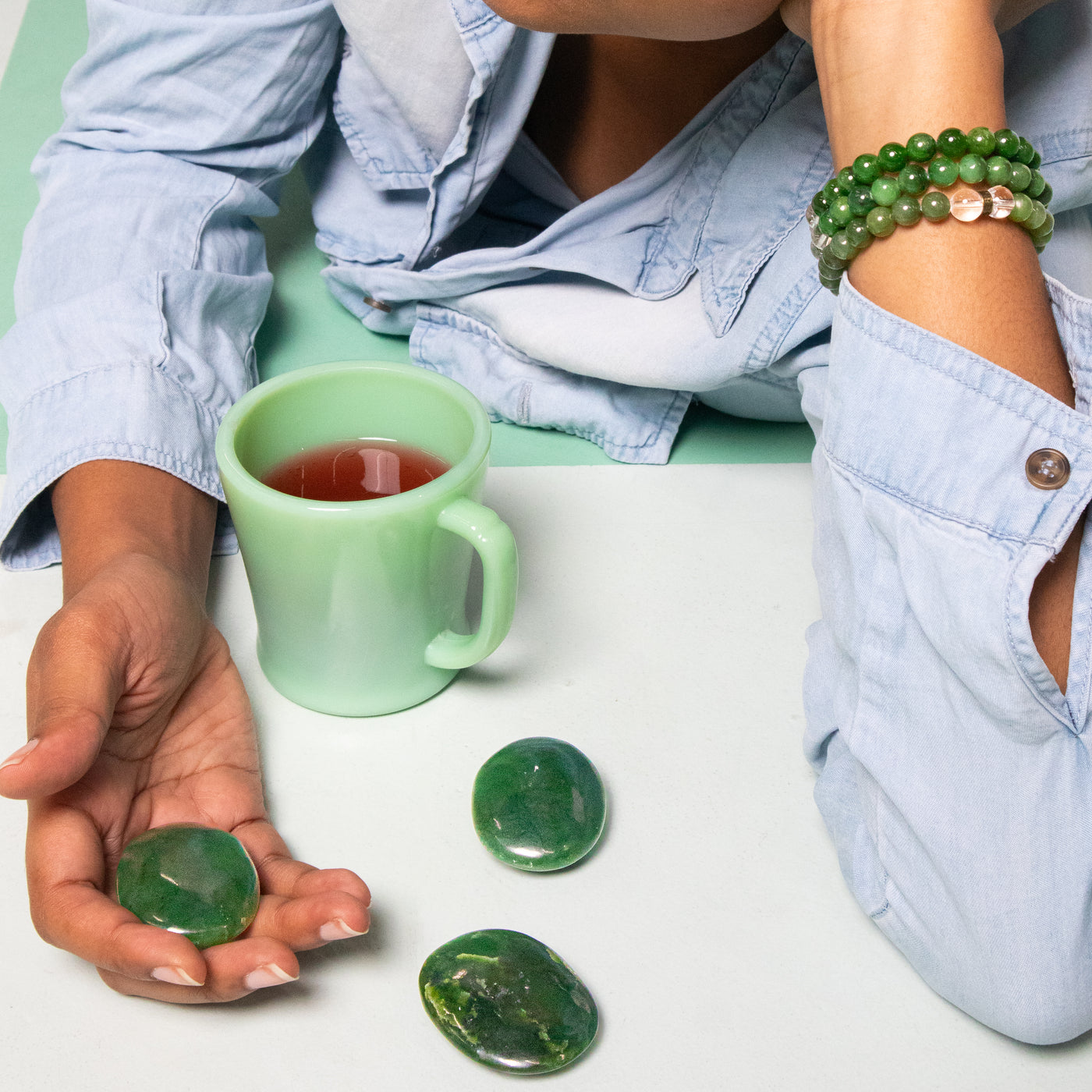 close up shot of woman wearing 3 jade bracelets, holding a jade touchstone and drinking green tea out of a jadeite glass mug by Energy Muse