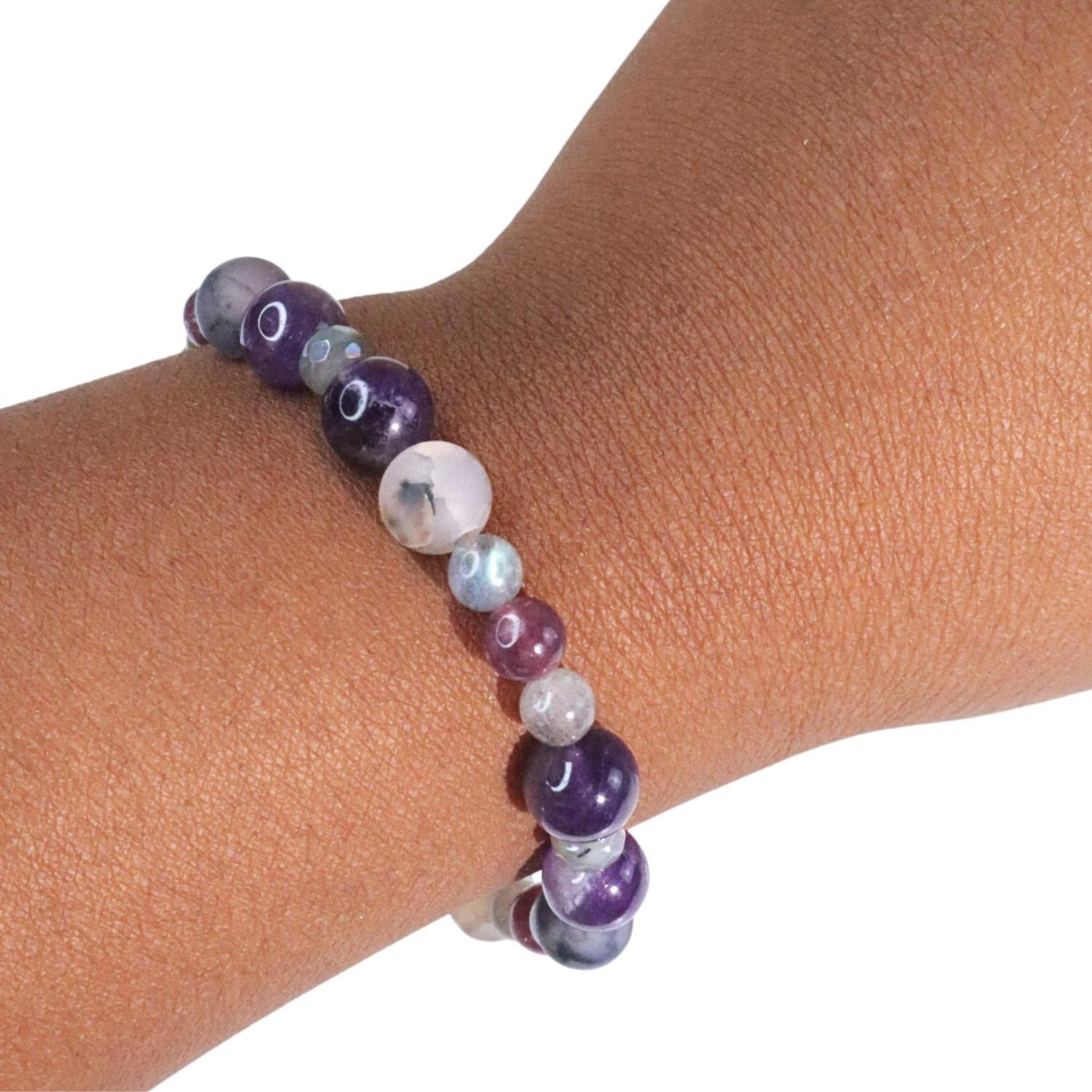 Young Black woman wearing new exclusive crystal formula Miracles Bracelet by Energy Muse featuring Amethyst, Lepidolite, Web Agate, Labradorite, and Aura Gray Moonstone on her left wrist.