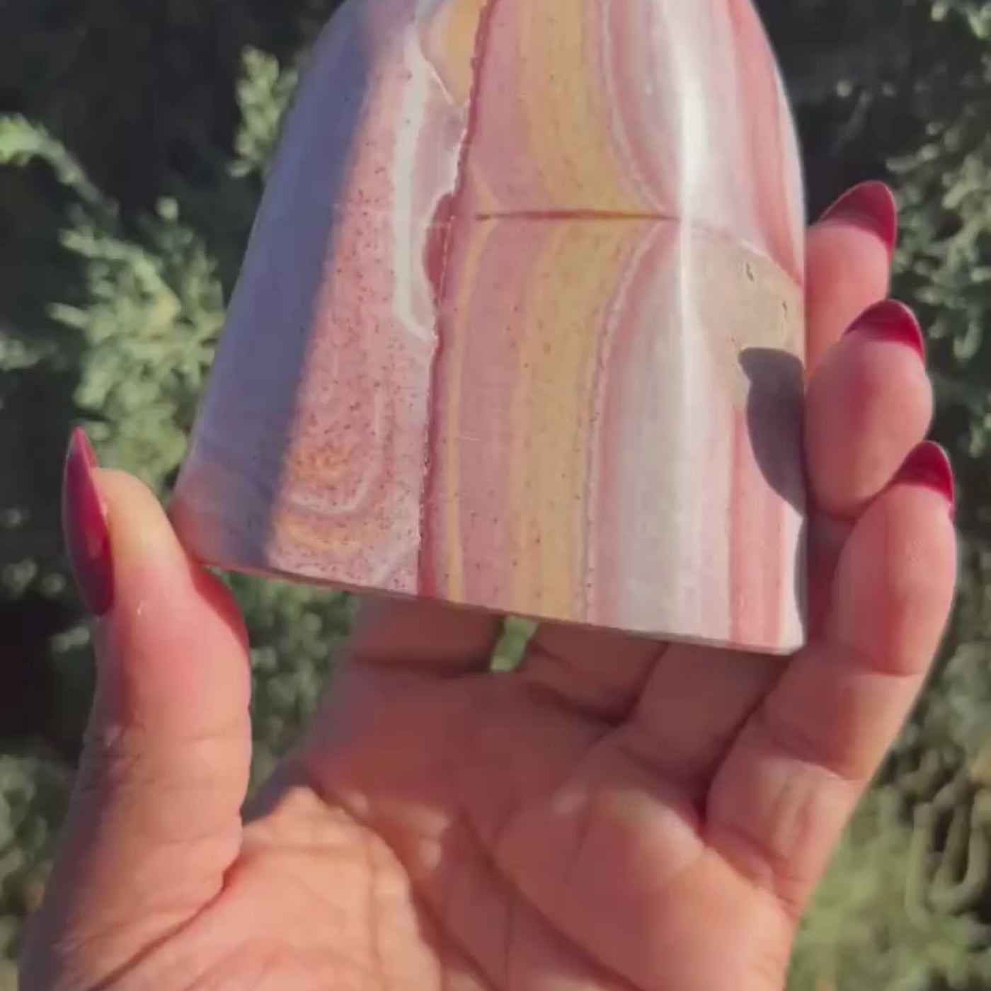Short video of woman holding up and turning around a Rainbow Rhyolite freeform crystal to show detail by Energy Muse