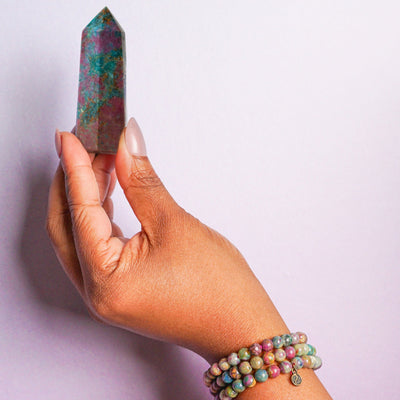 Black woman's hand wearing 3 genuine Ruby in Kyanite crystal bracelets and holding a Ruby in Kyanite point by Energy Muse