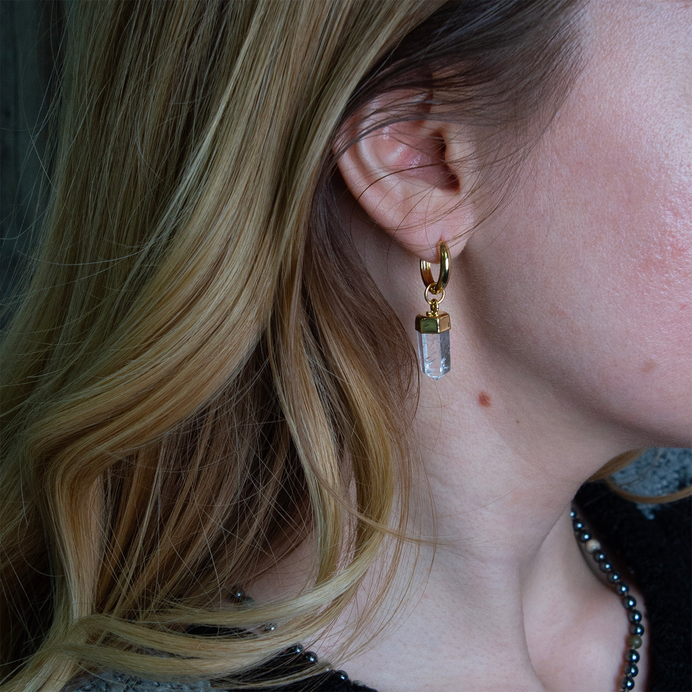 Woman wearing gold Clear Quartz point huggie drop earrings by Energy Muse