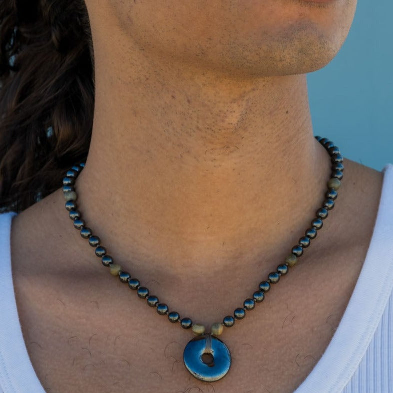 A young man of color wearing the Grounding Necklace by Energy Muse outside on the beach.
