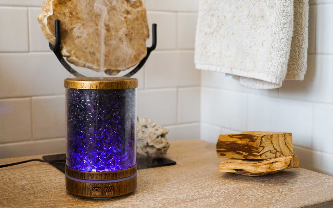 Amethyst-infused essential oil diffuser with internal light placed in clean bathroom by Energy Muse