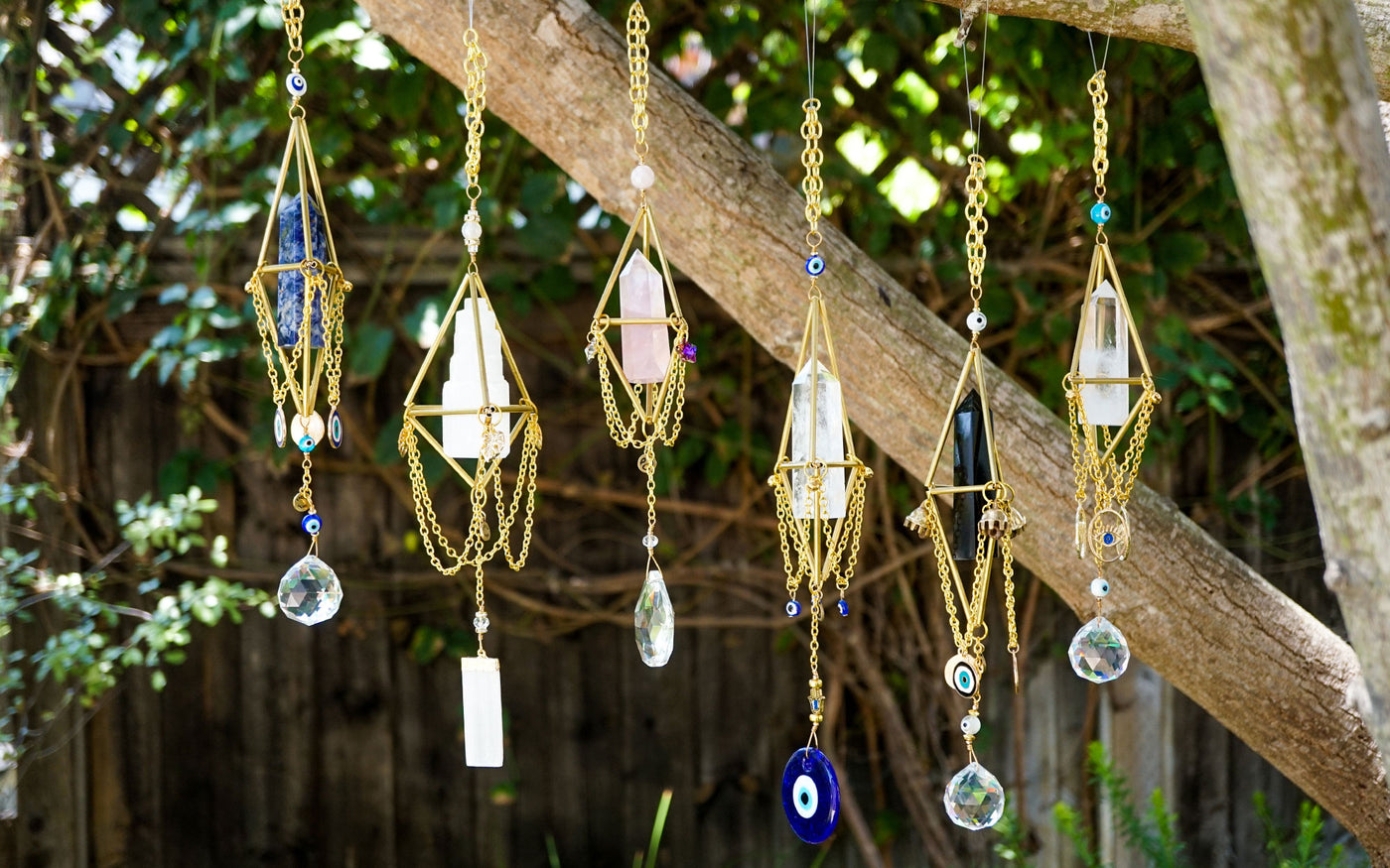 Group of 5 gold draped chain natural crystal chandeliers hanging on branch of a tree outside by Energy Muse