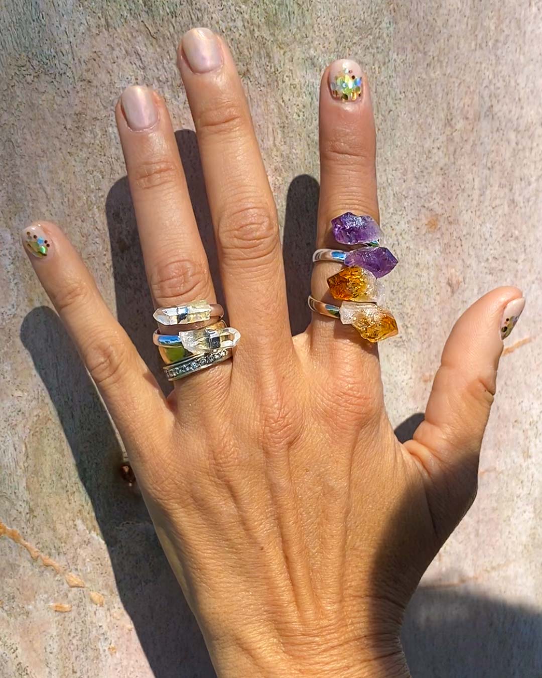 woman's left hand wearing amethyst crystal ring, citrine crystal ring and clear quartz ring 