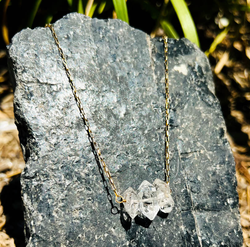 genuine Herkimer diamond gemstone necklace on gold-polished chain resting on black tourmaline outside by Energy Muse