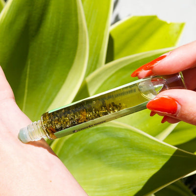 Woman rolling Money Magnet Oil Roller by Energy Muse featuring genuine Pyrite, Aventurine and Citrine crystals, plus organic cinnamon, five finger grass and basil oils on her left wrist. 