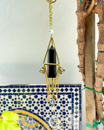 View of gold crystal chandelier with natural black obsidian point, bell charms, evil eye charms, clear crystal faceted prism ball outside by Energy Muse