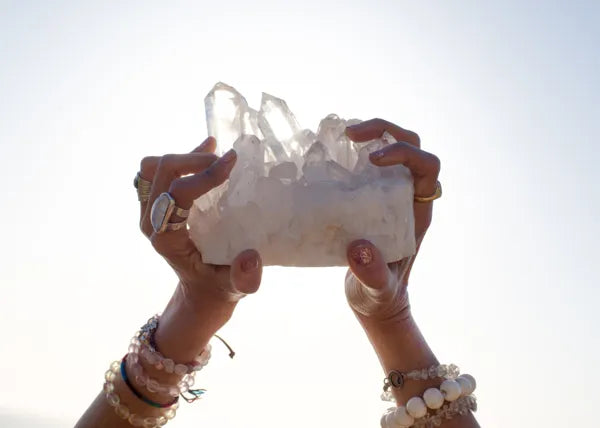 Two hands holding a quartz cluster up to the light