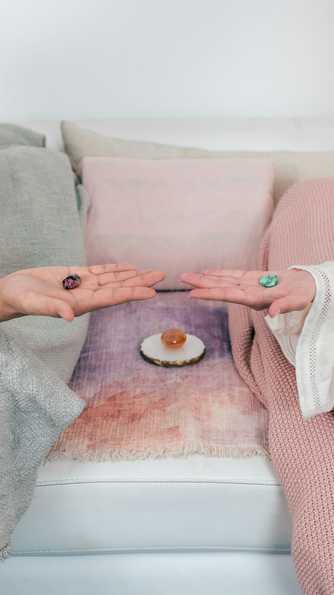 Two open hands holding crystals over a pink pillow